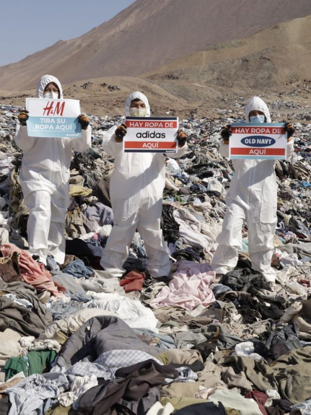 volunteers holding up signs that say H&M, adidas, and Old Navy amidst the clothing waste in Atacama Desert