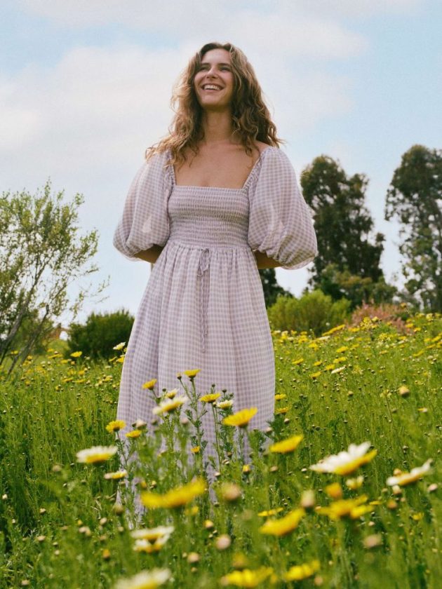 woman wearing purple sustainable dress in field of grass and flowers