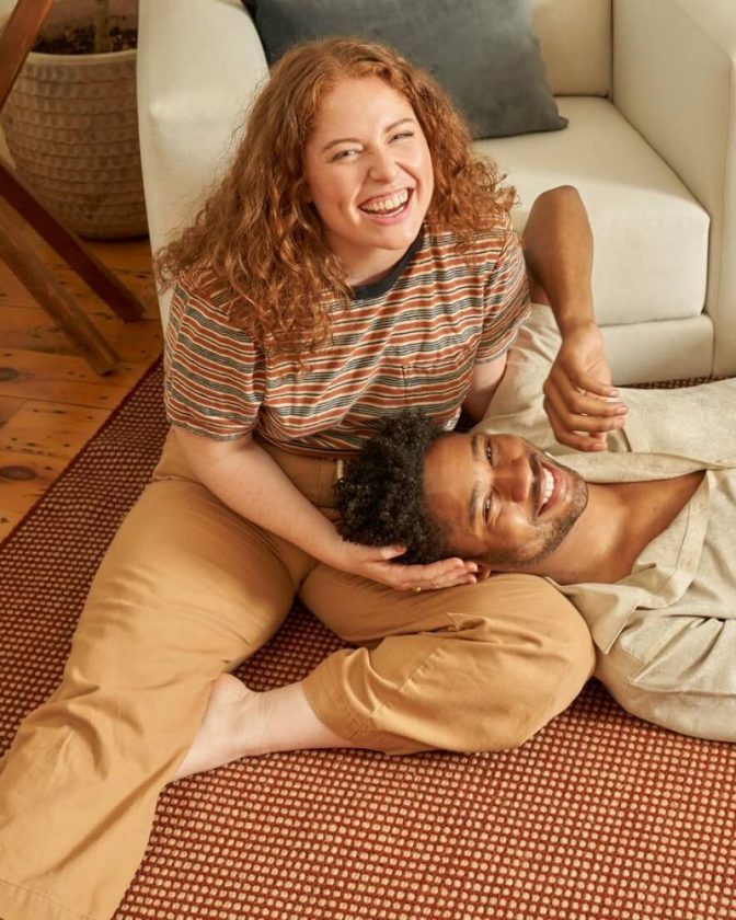 a man and woman sitting on a red sustainable rug made from wool and jute