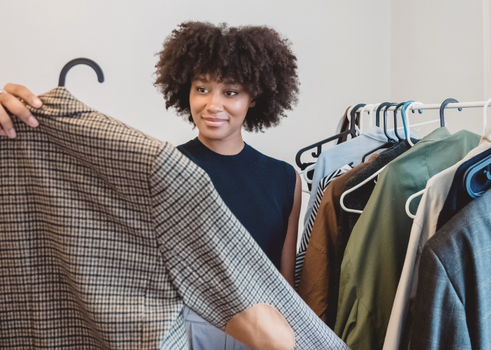 woman holding up blazer in front of rack of clothes - No New Clothes Challenges